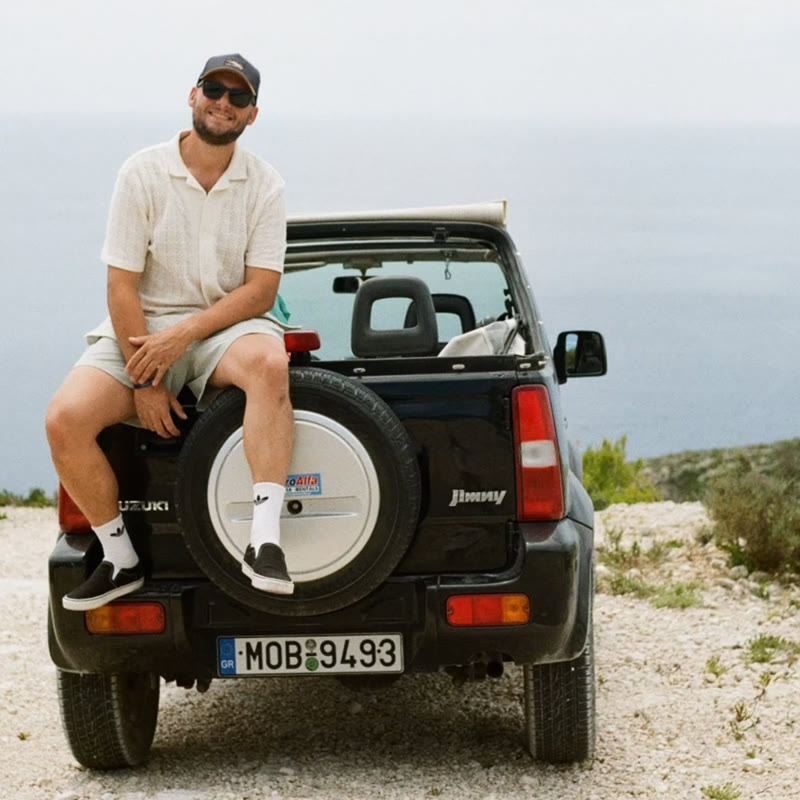 David sedí na černém Suzuki Jimny nad mořem